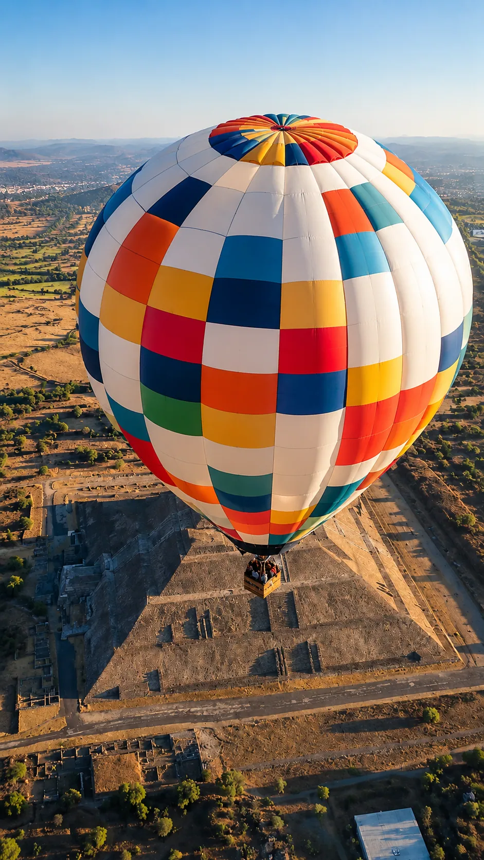 A colorful hot air balloon descending over a pyramid at Teotihuacán