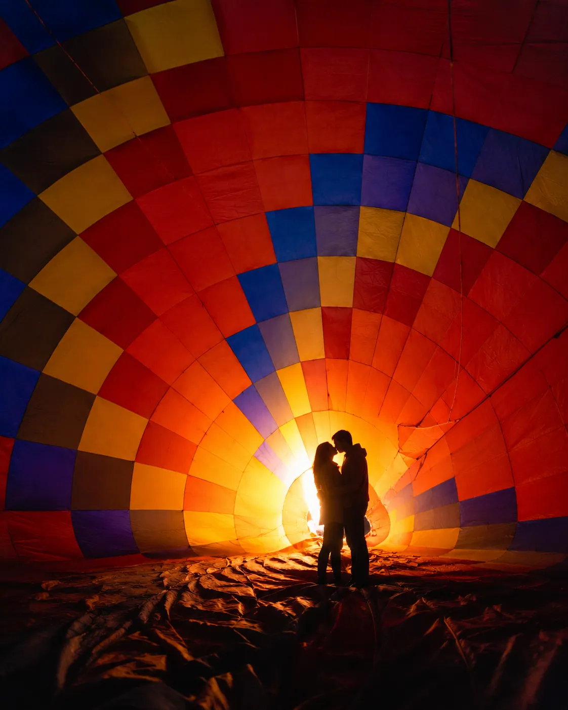 A couple silhouetted inside a colorful balloon envelope during inflation