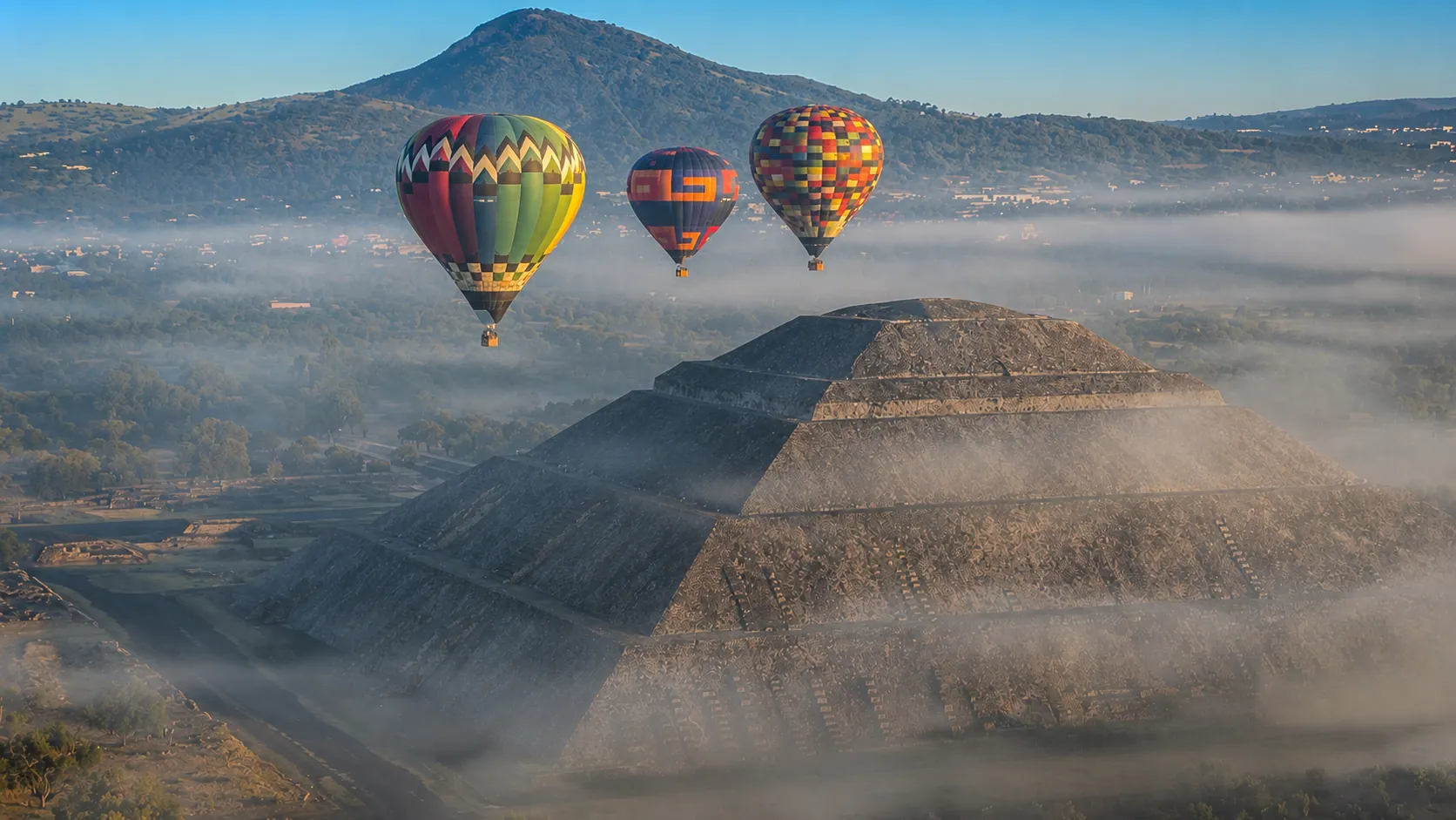 Three hot air balloons over the Pyramid of the Sun in morning mist
