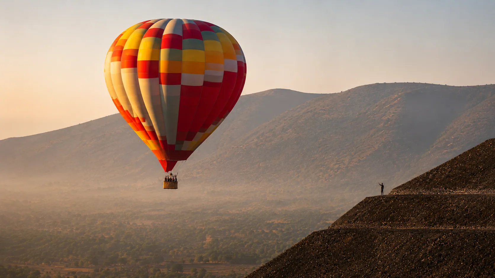 A single hot air balloon beside a pyramid in soft morning light